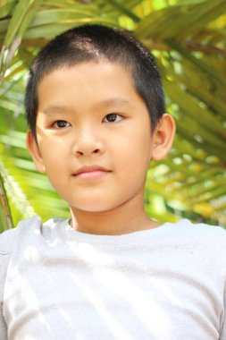 Çevresi parlak yeşillik ve benekli güneş ışığıyla çevrili çocukluk masumiyetini ve neşesini yakalayan düşünceli bir çocuğun portresi..