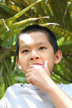 Gür tropikal bir ortamda bir anın tadını çıkaran düşünceli bir çocuk. Yüzündeki ifade, güneş ışığıyla aydınlatılan merak ve masumiyeti yansıtıyor..