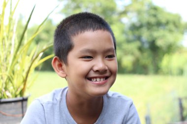 Neşeli genç bir çocuk, yemyeşil yemyeşil bir çevrede, doğal bir ortamda parlak bir şekilde gülümser. Onun ifadesi mutluluğu ve masumiyeti yansıtıyor..