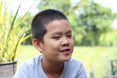 Çevresi yeşilliklerle çevrili neşeli genç bir çocuk doğal bir ortamda gülümsüyor. Neşeli ifadesi çocukluk mutluluğunun ve masumiyetinin özünü yansıtıyor..