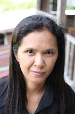 Uzun siyah saçlı, ciddi bir ifade sergileyen bir kadının yakın plan portresi. Bu görüntü, doğal bir ortamda sakin ve düşünceli bir anı yansıtır..