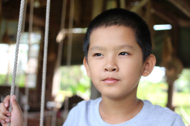 Salıncakta oturan genç bir çocuk, düşünceli bir ifade sergiliyor. Bu sakin açık hava sahnesi çocukluk ve tasasız anların özünü yakalar..