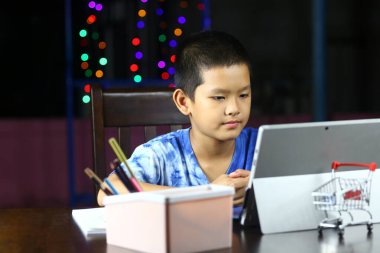 Odaklanmış bir çocuk evde renkli ışıklarla çevrili bir tabletle meşgul, modern teknolojiyi ve rahat bir ortamda öğrenmenin keyfini sergiliyor..