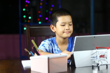 Kapalı bir ortamda tabletine odaklanmış genç bir çocuk. Yaratıcı atmosfer renkli ışıklarla gelişir, öğrenme ve oynama hissini teşvik eder..