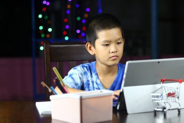Evde renkli ışıklarla çevrili tablet kullanan odaklanmış bir çocuk. Konsantrasyonunu ve yaratıcılığını kapalı bir ortamda göstererek öğrenme ve çalışma ile meşgul..