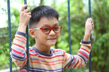 Gözlüklü çekici bir çocuk yemyeşil bir bahçede sallanmayı sever. Neşeli ifadesi çocukluk sevincinin ve kaygısız anların özünü yakalıyor..