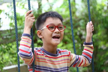 Neşeli bir çocuk yemyeşil bir bahçede sallanmaktan, saf mutluluk ve neşe dolu enerji göstermekten zevk alır. Parlak renkler ve doğa sahneye hayat getirir..