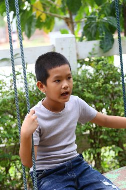 Genç bir çocuk yemyeşil bir bahçe ortamında sallanmaktan hoşlanıyor. Neşeli ifadesi çocukluk oyununun ve açık hava eğlencesinin özünü yansıtıyor..