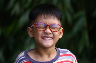 Gözlüklü neşeli bir genç açık havada gülümsüyor, yemyeşil ile çevrili. Neşeli ifadesi çocukluk mutluluğunun özünü yansıtıyor..