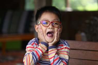 Gözlüklü neşeli bir çocuk evde otururken neşeli ve şaşırmış bir ifade sergiliyor. Neşeli atmosfer çocukluk hazzının özünü yakalar..