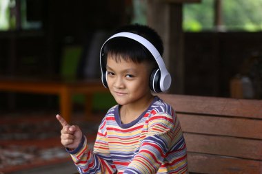 Neşeli bir çocuk kulaklıkla müzik dinlemekten hoşlanır, evde otururken neşeli bir yüz ifadesi sergiler. Renkli çizgili gömleği neşe ve masumiyeti yansıtan canlı atmosfere ekliyor..