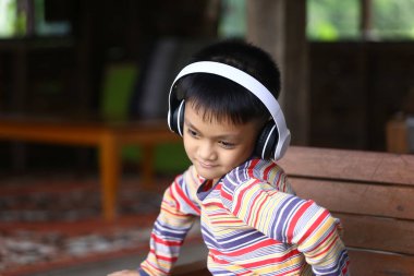 Neşeli bir çocuk evde rahatça otururken kulaklıkla müzik dinlemekten hoşlanır. Neşeli ifade ve renkli çizgili gömlek gençlik mutluluğu ve rahatlama anını yakalar..
