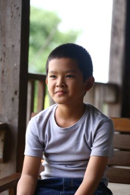 Neşeli bir çocuk ahşap bir bankta oturuyor, neşe ve masumiyet anı yakalıyor. Bu portre, açık havada gülümseyen bir çocuğu gösteriyor..