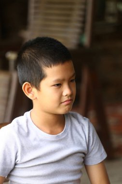 Düşünceli bir yüzü olan genç bir çocuk evde oturuyor, gri bir tişört giyiyor. Sakin tavrı ve rahat duruşu, çocukluk masumiyetini yakalamak için mükemmel bir iç gözlem anı oluşturuyor..