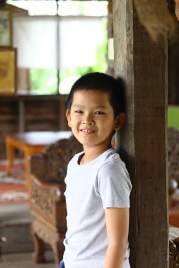 Neşeli genç bir çocuk geleneksel bir odada tahta bir sütuna yaslanırken gülümsüyor. Bu portre masumiyeti ve mutluluğu kapsıyor..