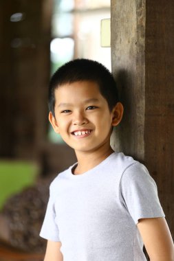 Neşeli genç bir çocuk ahşap bir direğe yaslanırken parlak bir şekilde gülümser. Neşeli ifadesi gençliğin ve mutluluğun özünü canlı ve kapalı bir ortamda yakalıyor..