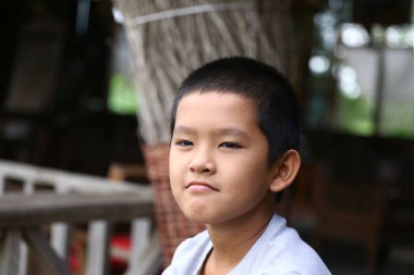 Kısa saçlı genç bir çocuk düşünceli bir şekilde oturur ve çeşitli duygular gösterir. Doğal ortam, bu samimi portredeki derin düşüncelere dalmasını sağlıyor..