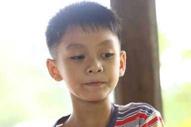 Düşünceli genç bir çocuk, hafif aydınlık bir çevrede bir anlık tefekkür görüntüsü yakalayarak uzaklığa bakar. Onun ciddi ifadesi masumiyeti ve merakı yansıtıyor..