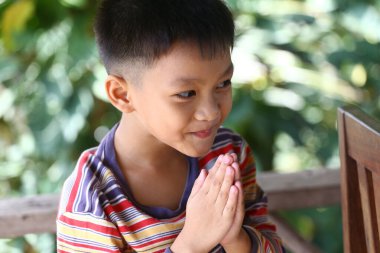 Neşeli genç bir çocuk, masumiyetini ve neşesini gösteren bir dua anında yakalanıyor. Bereketli yeşilliklerle çevrili, mutluluğu ve derin bir kültür duygusunu simgeliyor..