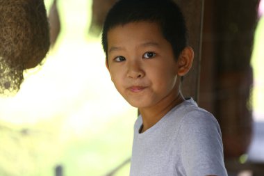 Genç bir çocuk açık havada neşeli bir şekilde gülümsüyor, doğal bir ortamda masumiyet ve neşe sergiliyor, yumuşak ışıklandırma ve canlı bir arka planla..