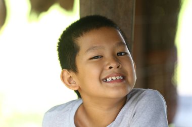 Neşeli genç bir çocuk açık havada eğlenirken parlak bir gülümseme sergiliyor. Neşeli ifadesi çocukluk masumiyetinin ve mutluluğunun özünü yansıtıyor..