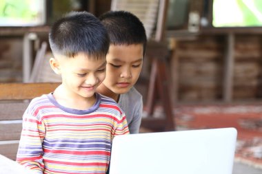 İki genç çocuk, teknolojinin ve öğrenmenin sevincini gösteren bir dizüstü bilgisayarla mutlu bir şekilde etkileşimde bulunuyorlar. Neşeli ifadeleri bir keşif ve dostluk anını yansıtır..