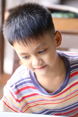 Çizgili tişörtlü genç bir çocuk evde eğlenirken gülümsüyor. Sıcak ışık ve ifadesi çocukluk keşiflerinde neşe ve merak taşır..