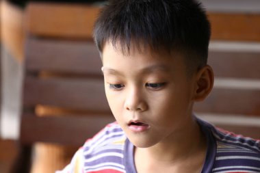 Düşünceli genç bir çocuk, odaklanmış bir ifadeyle, masumiyetini ve merakını, doğal ışıkta yakalanmış, sıradan çizgili bir gömlekle, mesafeye bakar..