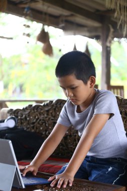 A young boy sits indoors, focused on his laptop, engaged in a digital task. The serene environment highlights his concentration and creativity. clipart