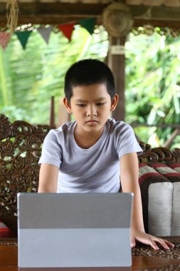 Genç bir çocuk rahat, doğal bir ortamda dikkatlice oturur, tabletle meşgul olur. Odağında teknoloji ve çocukluk eğitimi arasındaki etkileşim vurgulanıyor..