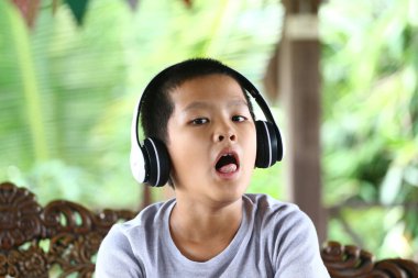 Kulaklık takan neşeli bir çocuk açık havada müzik dinliyor, doğal ortamında mutluluk ve rahatlığın canlı bir ifadesini sergiliyor..