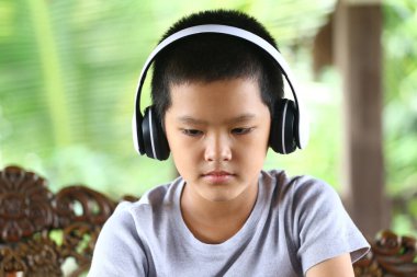 Kulaklık takan genç bir çocuk sessizce oturur, tamamen müziğiyle ilgilenir. Doğal yeşil zemin, bu anın rahatlatıcı atmosferini arttırır..
