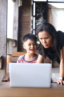 A joyful moment between a parent and child as they engage with a laptop at home. Their expressions reflect curiosity and excitement in a cozy indoor setting. clipart