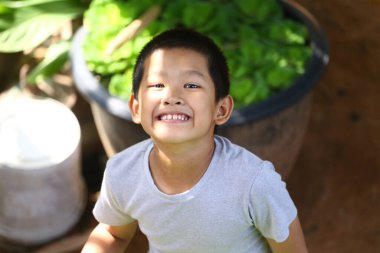 Neşeli genç bir çocuk, çevrenin yeşillikle çevrili olduğu doğal bir ortamda neşeli bir şekilde gülümser, masumiyeti ve mutluluğu oyuncu bir anda yakalar..