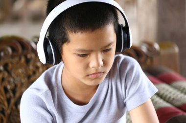 Kulaklık takmış, odaklanma ve konsantrasyon gösteren müziğe dalmış genç bir çocuk. Bu görüntü, gençliğin özünü sıradan, kapalı bir ortamda yakalar..