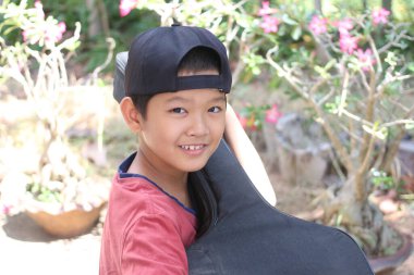 Neşeli bir çocuk açık havada, güzel çiçekler ve yeşilliklerle çevrili bir bahçede otururken parlak bir şekilde gülümsüyor..