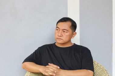 Düşünceli bir adam rahat bir şekilde oturur, düşüncelerini yansıtır. Tarafsız arka plan, ciddi ifadesini geliştirir, tefekkür havasını iletir..