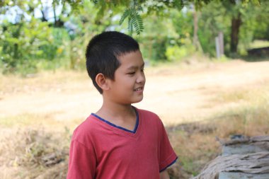 Açık havada gülümseyen neşeli bir genç çocuk çocukluk sevincini kucaklıyor. Sahne onun masumiyetini ve kaygısız ruhunu güneşli bir ortamda yakalıyor..