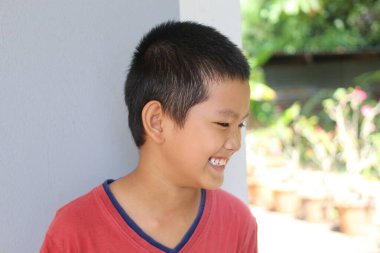 Neşeli genç bir çocuk açık hava ortamında parlak bir şekilde gülümsüyor, saf mutluluk sergiliyor. Neşeli ruhu ve pozitif enerjisi sıcak bir atmosfer yaratıyor..