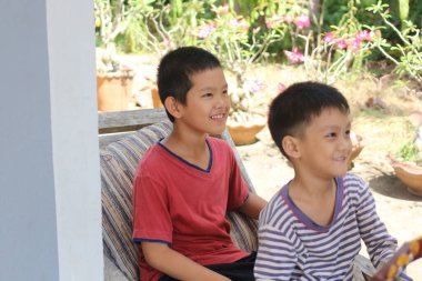 İki neşeli çocuk güneşli bir bahçede bir anlık kahkahayı paylaşıyorlar. Neşeli gülümsemeleri ve neşeli ifadeleri çocukluk sevincinin ve arkadaşlığın özünü yansıtır..