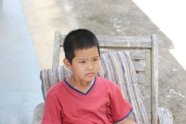 Dışarıdaki tahta sandalyede tek başına oturan genç bir çocuk, düşünceli bir şekilde gün ışığına yansıyor. Bu resim çocuklukta bir masumiyet ve tefekkür anını yakalar..