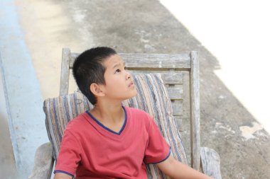 Düşünceli bir çocuk, açık hava ortamında oturmuş, düşüncelere dalıp masumiyetini yakalayan tuhaf bir ifadeyle yukarı bakar..