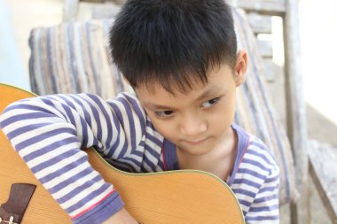 Düşünceli bir ifadeye sahip genç bir çocuk açık havada akustik gitar çalıyor, müzik ve yaratıcılığa olan sevgisini doğal ortamında sergiliyor..