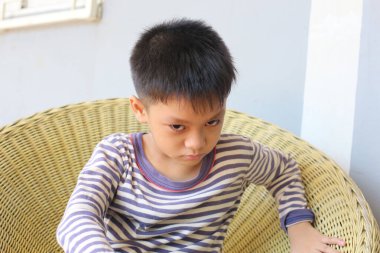 Genç bir çocuk rahat bir sandalyede otururken yoğun bir yüz ifadesi sergiler. Ciddi davranışı, çocukluk duygusunu yansıtan rahat iç mekan ortamına zıt düşüyor..