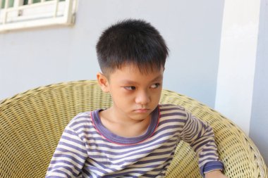 Genç bir çocuk hasır bir sandalyede otururken hoşnutsuz bir yüz ifadesi sergiliyor, çocukluk anılarını ve duygularını içeride yakalıyor..