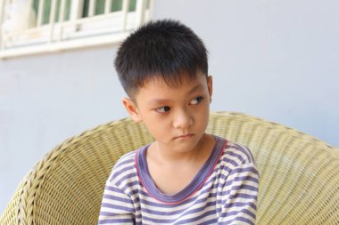 Düşünceli genç bir çocuk örülmüş bir sandalyede oturuyor, ciddi bir ifadeyle mesafeye bakıyor. Kapalı mekan, sessiz bir düşünce ve masumiyet hissi yakalıyor..