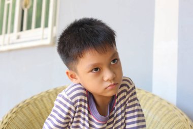 Düşünceli bir çocuk rahat bir hasır koltukta oturur ve sessizce içeri yansıtır. Düşünceli ifadesi çocukluk anılarını ve masumiyetini yansıtıyor..