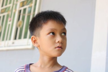 Genç bir çocuk düşünceli bir şekilde yan tarafa bakar, düşüncelere daldığı anı yakalar. Çocukluğun masumiyetini ve merakını vurgulayan sıradan bir gömlek giyiyor..