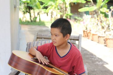 Genç bir çocuk açık havada gitarla oturup müziğe olan tutkusunu sergiliyor. Huzurlu bahçe arka planı bu sıcak günün rahat atmosferine ekleniyor..