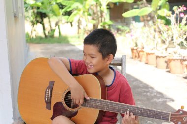 Neşeli bir çocuk açık havada akustik gitar çalıyor, canlı bir bahçede müziğe olan sevgisi ve yeteneğini gösteriyor..